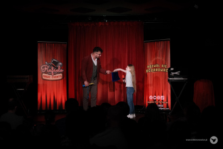 Dziewczynka losuje z kapelusza. Kapelusz trzyma w rękach magik.