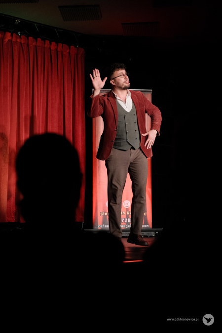 Magik macha do publiczności. Na pierwszym planie widać kontury osób na publiczności.