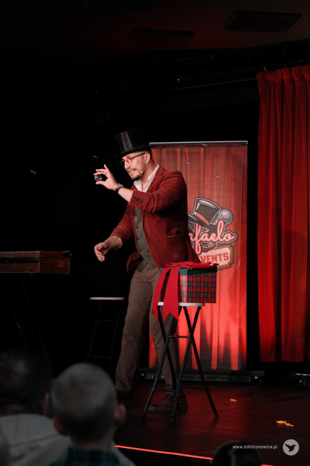 Magik pokazuje widowni małą przezroczystą kulę. Obok stoi mała skrzynka w czerwona kratkę.