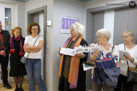 Galeria Przechodnia. Na środku stoi autorka prac Katarzyna Kate Bauer. Obok niej stoją kobiety. Jedna z nich trzyma razem z autorką długą książkę harmonijkową