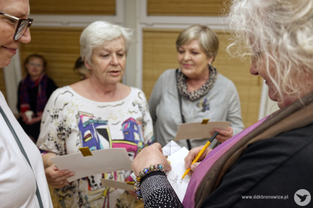 Katarzyna Kate Bauer składa autografy na małych obrazach. Obok niej stoją uśmiechnięte starsze uczestniczki wystawy.