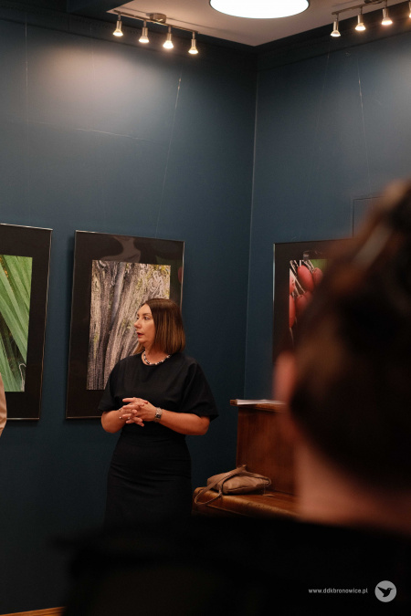 Na tle zawieszonych fotografii stoi w czarnej sukience Koordynatorka Galerii w Pasażu Aleksandra Machowska-Skrocka.