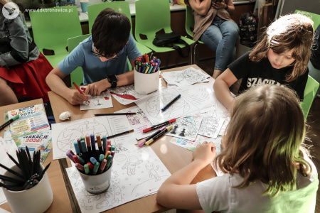 Dzieci kolorują kolorowanki z motywami szachowymi. Kolorowanki wyłożone są na stole. W pojemnikach widać flamastry.