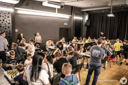 Sala widowiskowa wypełniona stołami i graczami. Widać również dopingujących rodziców.