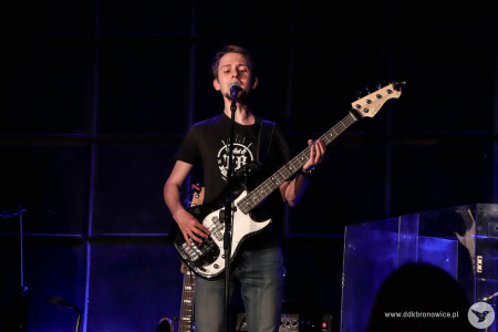 Gitarzysta basowy śpiewa do stojącego mikrofonu na scenie.