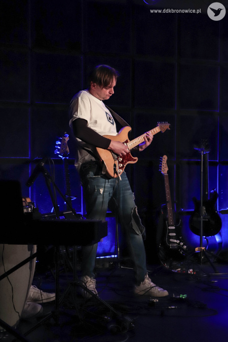 Mężczyzna w białej koszulce gra na gitarze.