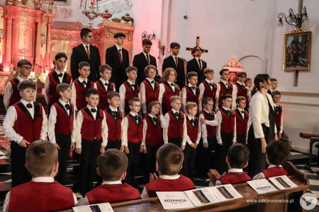 Występ Chóru Chłopięcego „Słowiki Lubelskie". Chórzyści ubrani są w czerwone kamizelki, muchy i białe koszule. Tworzą trzy rzędy, gdzie najwyżsi zajęli ostatni rząd. Najwyżsi mają czerwone krawaty i czarne marynarki.