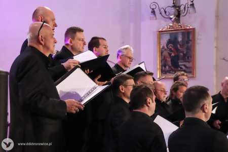 Zespół Męski KAIROS wykonuje pieśń. Ustawieni są w dwa rzędy. Za nimi złote elementy kościoła podkreśla fioletowe światło.