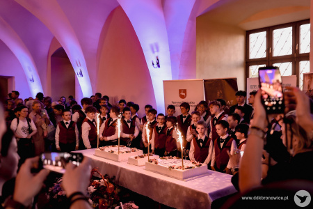 Pomieszczenie w klasztorze ojców dominikanów. Chór Chłopięcy Słowiki Lubelskie stoją przed wielkim tortem. Białe ściany podświetlone są niebieskimi światłami.