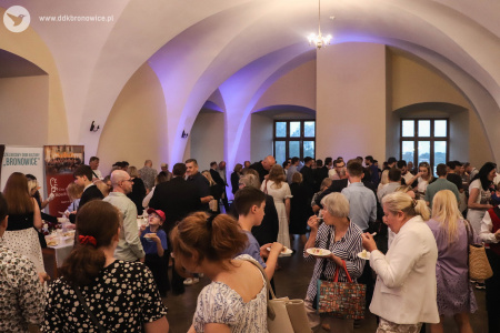 W pomieszczeniu goście częstują się tortem. Białe ściany podkreślone niebieskim światłem.