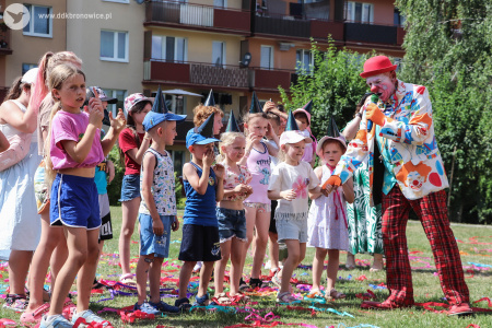 Dzieci bawią się i uśmiechają. Klaun w czerwonym meloniku bierze za rękę dziewczynkę.