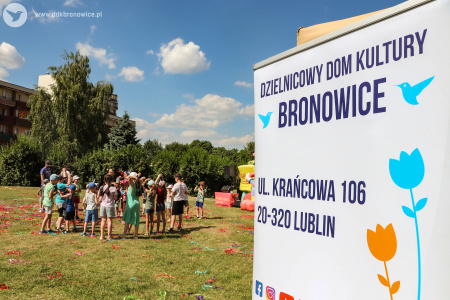 W tle dzieci bawia się z klaunami. Po prawej stronie widać biały plakat. Na nim napis: DZIELNICOWY DOM KULTURY BRONOWICE.