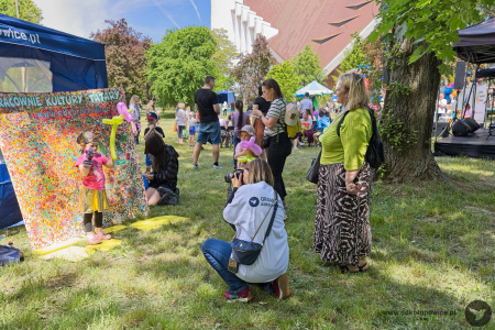 Na tle kolorowego obrazu z napisem: Pracownie Kultury Tatary dziewczynka robi zdjęcie. Zdjęcie robi kobieta z aparatem, w białej koszulce z napisem: organizator DDK Bronowice.