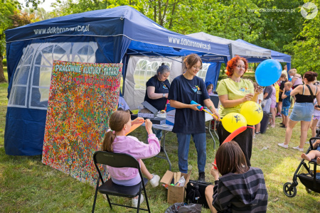 Dwie pracowniczki DDK Bronowice nadmuchują kolorowe balony. Po lewej stronie widać kolorowy obraz z napisem: Pracownie Kultury Tatary.