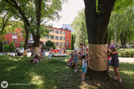 Na pniach rozwieszony papier. Dzieci rysują na nim kwiaty.