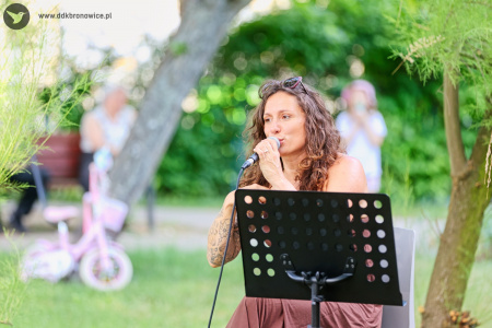 Sylvetta w brązowej sukience śpiewa piosenkę. Trzyma mikrofon.