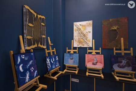 Przy granatowej ścianie Galerii w pasażu stoją na sztalugach obrazy. Trzy największe wiszą na ścianie.