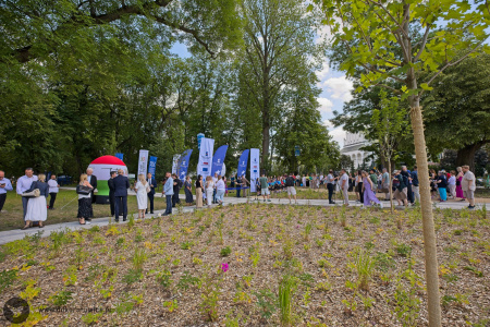 Mieszkańcy rozmawiają i spacerują po parku. W tle widać flagi sponsorów.