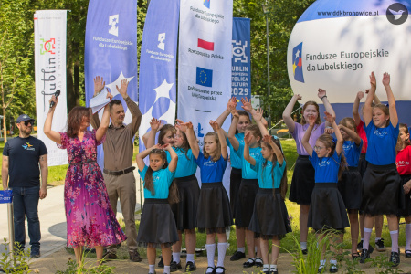 Dziewczynki w kolorowych koszulkach, z napisem: DO-RE-MI, podnoszą wysoko ręce. Uśmiechają się. Po lewej stronie stoi Łukasz Drozd, kierownik programowy Dzielnicowego Domu Kultury „Bronowice".