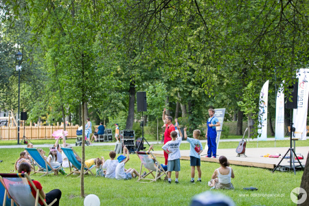 Dwóch aktorów ubranych na czerwono i niebiesko graja spektakl dla dzieci na drewnianej scenie.