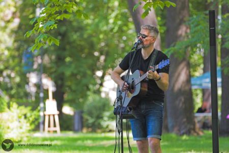 Muzyk w ciemnych okularach gra na gitarze do mikrofonu.