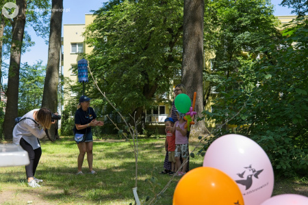 Kobieta i dwójka dzieci ustawiają się do zdjęcia. Po lewej stronie kobieta w jasnej koszulce robi im zdjęcie.