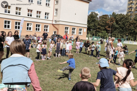 Na boisku dzieci robią rozgrzewkę ruchową. Stoją w kółku, w środku chłopiec prowadzi ćwiczenie, które pozostałe dzieci muszą wykonywać.