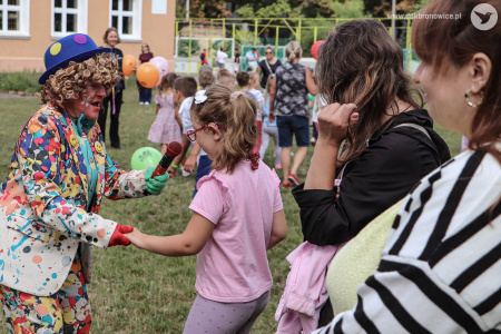 Klaun w niebieskim meloniku i jasnym garniturze rozmawia z małą dziewczynką.