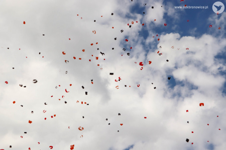 W powietrzu unosi się kolorowe confetti na tle niebieskiego nieba i białych chmur.