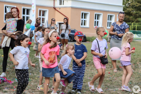 Grupka dzieci ma założone czerwone, klaunowe nosy i skaczą. W tle rodzice stoją z mniejszymi dziećmi.