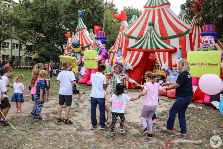 Dyrektor Aleksandra Szulc-Choma tańczy z grupką dzieci. Obok nich stoi klaun w niebieskim meloniku.