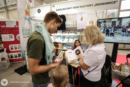 Autorka książek Urszula Lewartowicz podpisuje egzemplarze swoich książek. Obok Aleksandra Szulc-Choma przekazuje książkę mężczyźnie.
