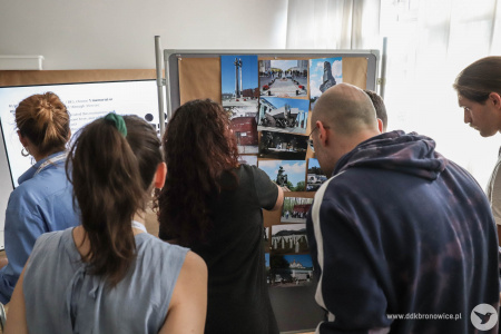 Uczestnicy jednych warsztatów oglądają wystawione na tablicy korkowej zdjęcia fotograficzne.