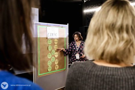Marta Gawinek-Dagargulia wyjaśnia uczestnikom plan dnia zawieszony na tablicy korkowej.