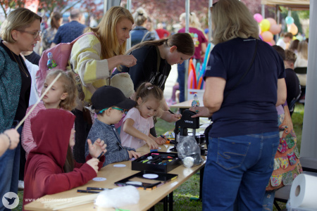 Stoisko warsztatowe. Przy stoisku stoi Aleksandra Szulc-Choma. Przed stoiskiem stoi duża grupa dzieci.