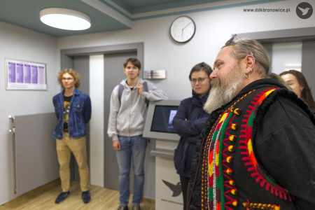 Opiekun artystyczny Grzegorz Nowicki przemawia do zebranych uczestników wystawy. Ma założoną kolorową kamizelkę.