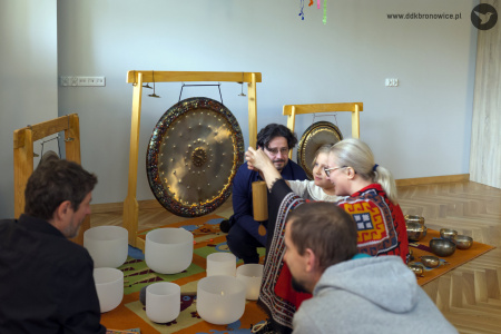 Wokół artystów siedzą dzieci. Uczą się grać na instrumentach. Artyści im pomagają. Dzieci mogą dotknąć instrumentów lub zagrać dźwięki.