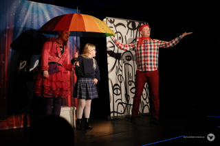 Grafika promująca spektakl w ramach cyklu Nove Poranki. Na tle czerwono-białej szachownicy, od lewego górnego rogu do prawego dolnego, rozciąga się białe pole. W lewym górnym rogu na białym tle, czarny napis: “NOVE PORANKI”. Litera “V” jest koloru czerwonego, a pod nim mały, niebieski napis: “SCENA FAMILIJNA”. W środkowej części grafiki fioletowo-czerwony napis: “O PCHLE, CO MANIER NIE MIAŁA” pod nim dwie kreski. Po lewej stronie, obok tytułu, fragment zdjęcia aktorki w kostiumie pchły - fioletowy żakiet, granatowa sukienka i czerwony kwiat we włosach. W prawym dolnym rogu szary napis www.ddkbronowice.pl, obok napisu mały koliber na szarym tle.