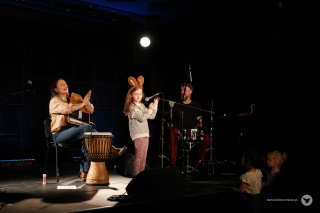 Grafika promująca koncert w ramach cyklu Nove Poranki. Na tle zielono-białej szachownicy, od lewego górnego rogu do prawego dolnego, rozciąga się białe pole. W lewym górnym rogu na białym tle, czarny napis: “NOVE PORANKI”. Litera “V” jest koloru zielonego, a pod nim mały, pomarańczowy napis: “SCENA FAMILIJNA”. W środkowej części grafiki pomarańczowy napis: “NATURA GRA!”, pod nim w kolorze zielonym: “KONCERT ZESPOŁU DEFICYT NATURY” “SYLWIA LASOK, MARCIN KOWALCZUK, MARCIN KISIEL”. Obok każdy z artystów ukazany w formie małego, okrągłego zdjęcia. W lewej części grafiki, obok napisów, instrumenty muzyczne obrośnięte bluszczem, kwiatami i owocami. W prawym dolnym rogu szary napis www.ddkbronowice.pl, obok napisu mały koliber na szarym tle.