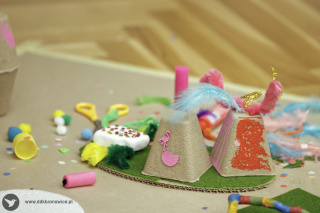 Grafika promująca spotkanie z cyklu Twórcza Pracownia. Grafikę stanowi zdjęcie jasnych kamieni. Na nich położone są goździki, pomarańczowe pióro i laski cynamonu. W środkowej części zdjęcia leży figurka słonia mieniącego się na fioletowo, niebiesko i zielono. W lewej górnej części grafiki, logotyp Twórczej Pracowni - rozlany kleks farb żółtej, niebieskiej i zielonej, tworzy kształt korony. W jej środkowej części biała dłoń, a w niej jeszcze mniejsza, zielona. W prawym dolnym rogu szary napis www.ddkbronowice.pl, obok napisu mały koliber na szarym tle.