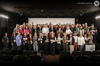 Grafika promująca międzynarodowe forum. Grafikę stanowi zdjęcie uczestników. Duża grupa osób pozuje do wspólnego zdjęcia w dużej sali. Trzymają kolorowe banery i są uśmiechnięci. W lewym dolnym rogu na jasnym tle napis: „TRIYOU FORUM: Exchange, Engage, Empower” oraz obok „Apply now!”. Niżej mniejszy napis: „28-30 SEPTEMBER 2026, Lublin”. Na dole grafiki na samym dole grafiki, na jasnym tle logotypy organizatorów.