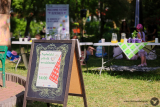 GRafika promująca piknik z okazji 3. urodzin Pracowni Kultury Dziesiąta. Grafikę stanowi w większości białe tło. W lewym dolnym rogu tło ma kształt biało-czerwonego koca piknikowego. Na białym tle zielony napis: „SĄSIEDZKI PIKNIK URODZINOWY”. W literach widać źdźbła trawy. Obok widać od góry dwa kubki z kawą. Na jednym widać kształt kolibra, a na drugim liczbę 3. W lewym dolnym rogu napis: www.ddkbronowice.pl, obok napisu mały koliber na szarym tle.
